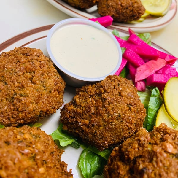Le Kabob's falafel plate with golden-brown falafel, white sauce, pink pickled turnips, and green lettuce.
