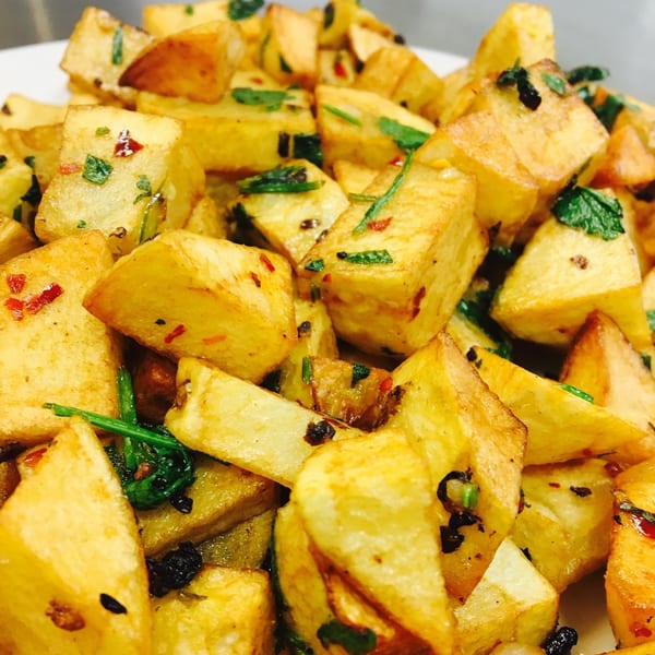 Close-up of golden fried potatoes, seasoned with green herbs and red pepper flakes.