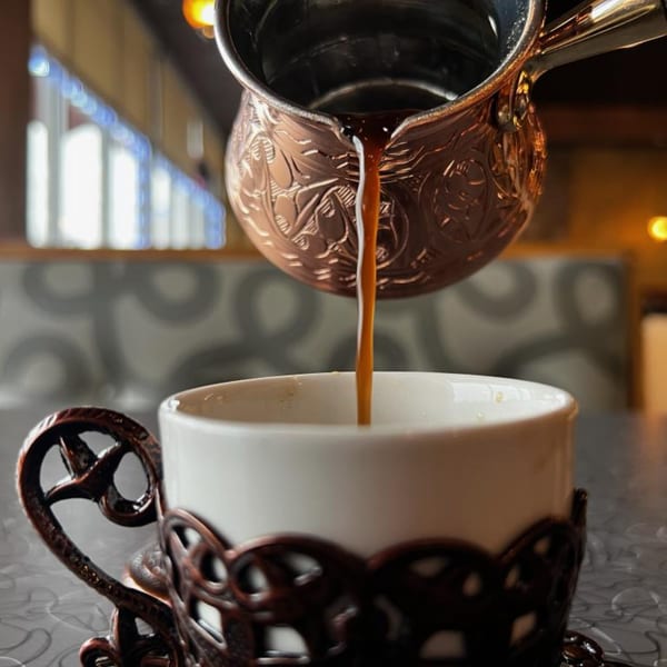 Rich, dark Turkish coffee pours from an ornate copper cezve into a white cup at Le Kabob.