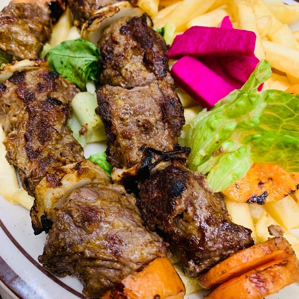 Le Kabob's grilled meat skewers with fries, pickled turnips, and fresh lettuce on a plate.