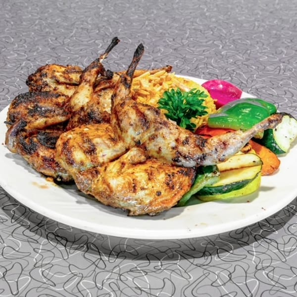 Grilled quail with rice, parsley, pickled turnips, and grilled vegetables on a white plate.