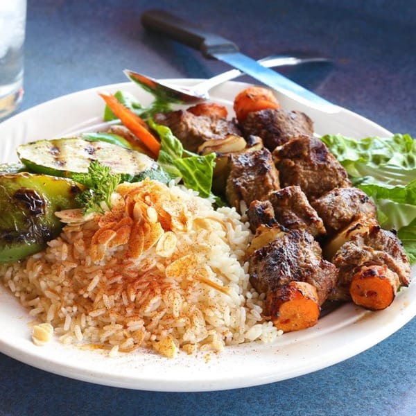 Le Kabob's Mediterranean beef shish kabob with rice, grilled vegetables, and fresh greens.